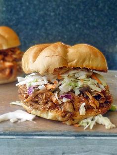 two pulled pork sandwiches with coleslaw and slaw on a wooden cutting board