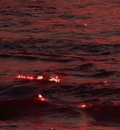 the sun is setting over the ocean with red lights in the water and small waves