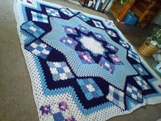 a blue and white crocheted afghan on the floor in front of a bookshelf