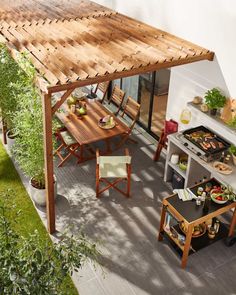 an outdoor kitchen and dining area with wooden table, chairs and grill on the patio