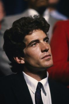 a close up of a person wearing a suit and tie with other people in the background