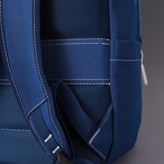 a blue backpack with white stitching on the front and back straps, sitting against a gray background