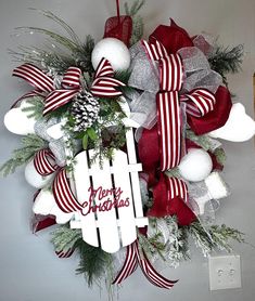 a christmas wreath hanging on the wall with red and white ribbons, evergreens and ornaments