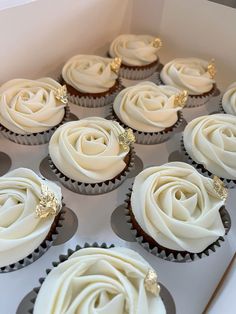 cupcakes with white frosting and gold decorations are in a box on the table