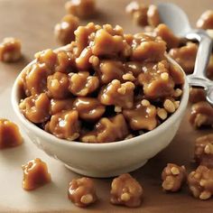 a bowl filled with caramel nuts on top of a wooden table next to spoons