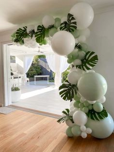 balloon arch with white and green balloons in front of an open door at the entrance to a house