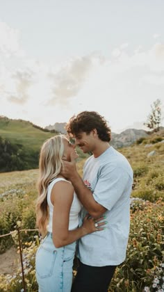 a man and woman standing next to each other in a field with wildflowers