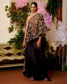 Feel the Summer breeze in this one-shoulder kaftan set. The cape is worn over a halter-neck gold top which appears as if it was dipped in gold while the black cape carries a bouquet of flowers embroidered on it. The flowy and comfortable pants and top together look regal as well as flowy to beat the heat. Halterneck blouse with a dori for closure at the back. Floral embroidered one-shoulder black cape. Basic black pants come with a simple flowy look and an SS concealed zip for a seamless look. F Cape And Pants, Halterneck Blouse, Organza Butterfly, Kaftan Set, Cape Outfit, Cape Top, Black Kaftan, Modern Suits, Pants And Top