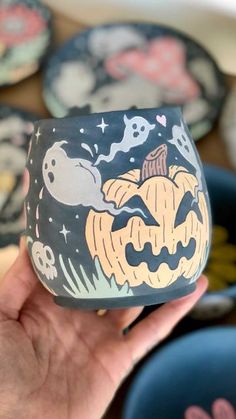 a hand holding up a halloween themed cupcake in front of plates with ghost and pumpkins on them