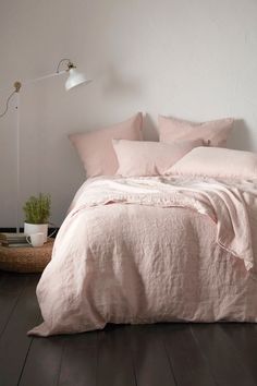 a bed with pink linens and pillows in a white room next to a lamp