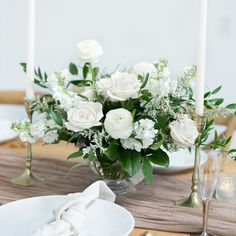 white flowers in a vase on a table with silverware and napkins next to candles