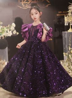 Acquiring a sense of majestic elegance is effortless with this stunning flower girl dress. The dress features a deep purple sequin-covered bodice that sparkles with every movement, making it a dazzling choice for any special occasion. The dramatic ruffled satin sleeves provide a regal touch, while the intricate beadwork at the neckline adds an extra layer of sophistication. The voluminous skirt flows beautifully, allowing for graceful movement and plenty of twirling. Perfect for weddings, pageants, or any formal event, this dress is designed to make a lasting impression. The high-quality construction ensures durability and comfort, with a soft inner lining that will keep your little one comfortable all day long. An easy-to-use zipper and adjustable fit make dressing simple and convenient. Purple Princess Dress With Sequins, Princess Style Purple Sequin Dress, Purple Sequined Princess Dress, Elegant Purple Princess Dress For Prom, Purple Tulle Dresses With Sequins, Purple Embellished Ball Gown For Party, Embellished Purple Ball Gown For Party, Purple Fitted Pageant Dress For Party, Fitted Purple Pageant Dress For Party