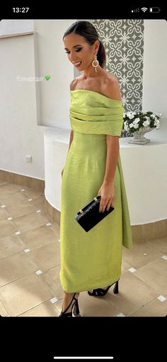 a woman in a lime green dress holding a black purse and posing for the camera