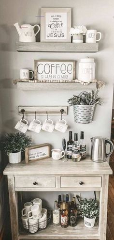 a coffee bar with cups and mugs on the shelves above it is decorated with greenery