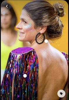 a woman with her back to the camera wearing colorful clothing and large hoop earrings, standing in front of a yellow wall