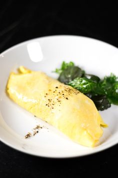 an omelet is on a white plate with greens