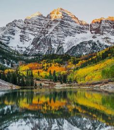 the mountains are covered in snow and fall colors as they reflect in the still water