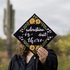 a woman wearing a graduation cap that says adventure is out there with sunflowers on it