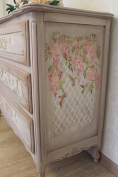 an old dresser with pink flowers painted on the front and side drawers, along with a vase filled with flowers