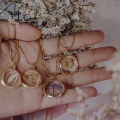 a person holding four different necklaces in their hand next to some white and brown flowers