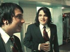 two men dressed in suits and ties are talking to each other while holding drinks together