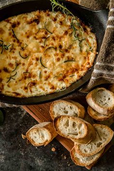 a skillet filled with cheese and bread on top of a wooden cutting board next to sliced