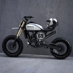 a white and black dirt bike parked in front of a gray wall with the number 69 on it