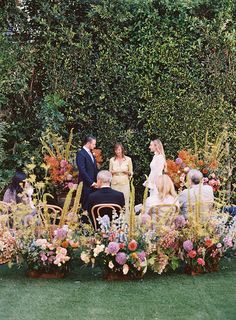 a group of people sitting around a table with flowers in front of them on the grass