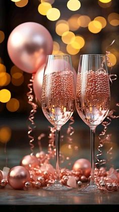 two champagne flutes with pink and gold decorations on the table in front of christmas lights