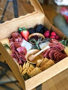 a box filled with assorted meats, cheese and fruit on top of a wooden table