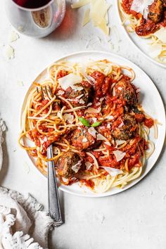 two plates of spaghetti with meatballs and sauce next to a glass of red wine