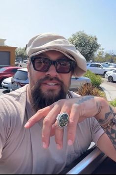 a man with glasses and a ring on his finger in front of a parking lot