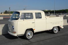 an old white truck is parked in a parking lot near a concrete wall and fence