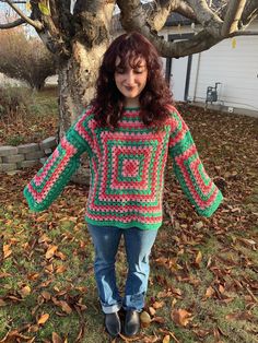 a woman standing in front of a tree wearing a colorful sweater