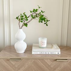 a white vase sitting on top of a wooden table next to a book and candle