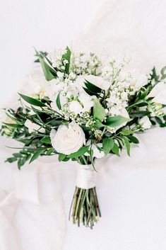 a bridal bouquet with white flowers and greenery on a white cloth draped over it