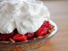 a dessert with whipped cream and strawberries in a glass dish on a wooden table