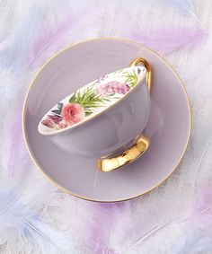 a cup and saucer on a plate with purple feathers around it that have flowers painted on them