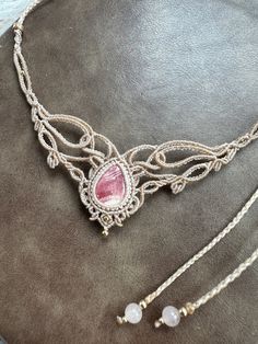 a necklace with a pink stone on it sitting on top of a table next to a pair of earrings