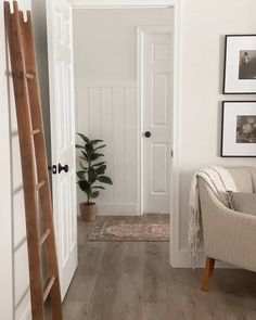 a living room with white walls and wood flooring next to a ladder leading up to the door