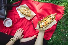 a person holding a hot dog on top of a red blanket