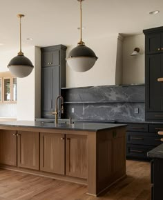 a large kitchen with wooden floors and black cabinets, two pendant lights over the island