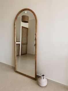 a mirror sitting on the floor next to a white vase and wall with a lamp in it