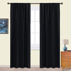 black curtains hanging in front of a window with white walls and wooden dresser next to it