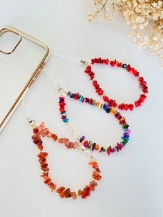 two colorful beaded necklaces sitting next to a cell phone on a white surface