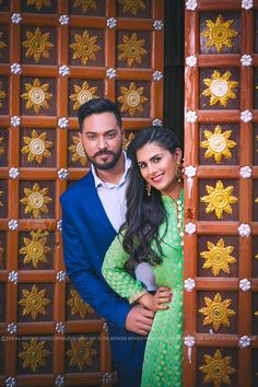 a man and woman standing next to each other in front of a wooden wall with gold decorations