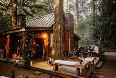 a cabin in the woods is lit up by lights and people are sitting on wooden benches