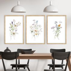 three framed art prints on the wall above a dining room table with two chairs and a vase