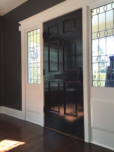 an empty room with a black door and stained glass window on the wall, along with hardwood flooring