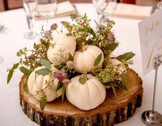 pumpkins and greenery are arranged on a wood slice at the center of a table